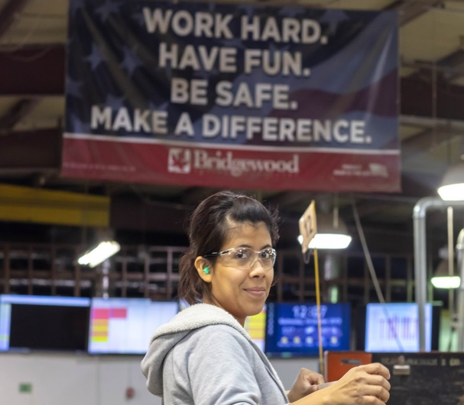 Bridgewood employee wearing safety glasses and earplugs smiling for photo while working