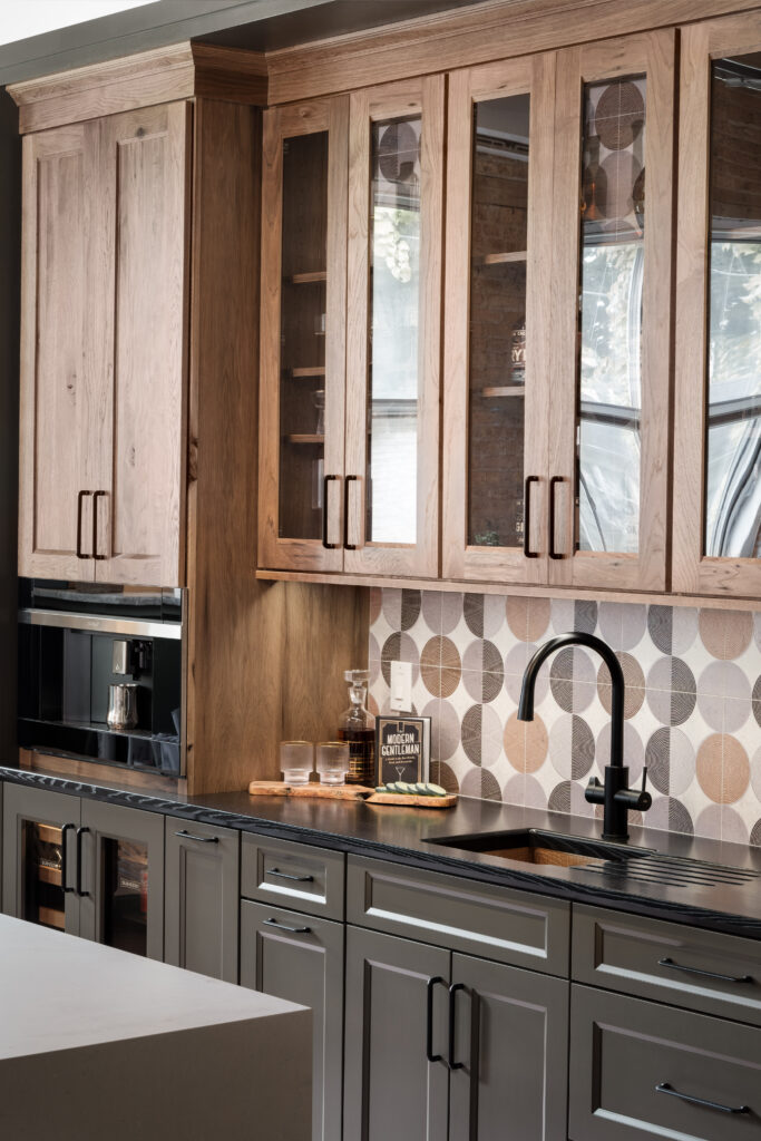 Kitchen with upper cabinetry made of hickory with with an aged finish and lower cabinetry made of maple painted urban bronze. Both sets match with embry styled doors featuring full doors and door frames with glass.